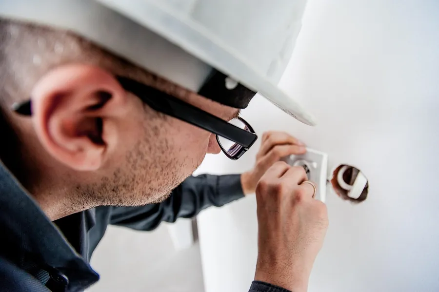 Eletricista instalando tomada elétrica de parede com capacete e óculos de proteção