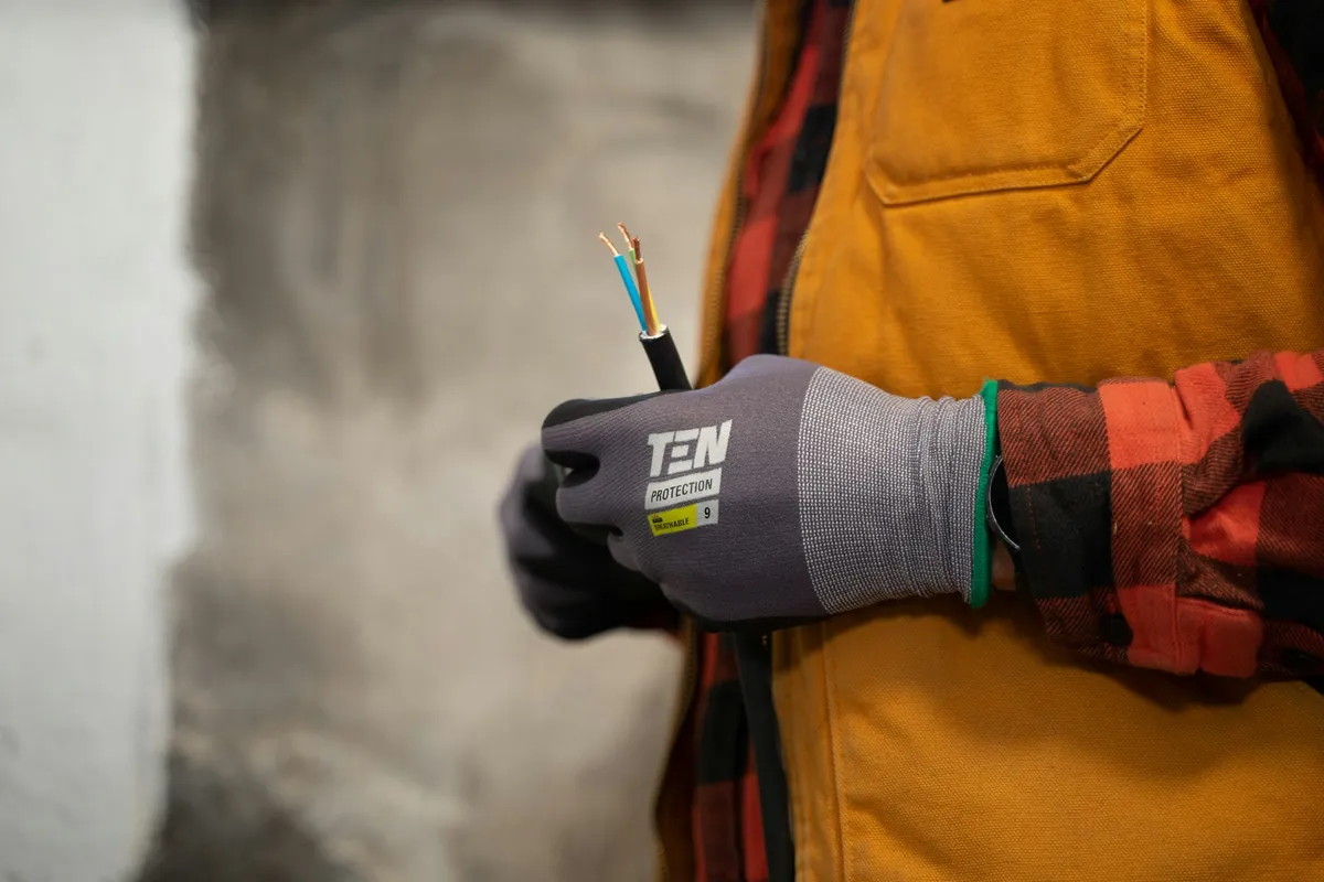 Eletricista manuseando fios elétricos com luva de proteção durante manutenção residencial